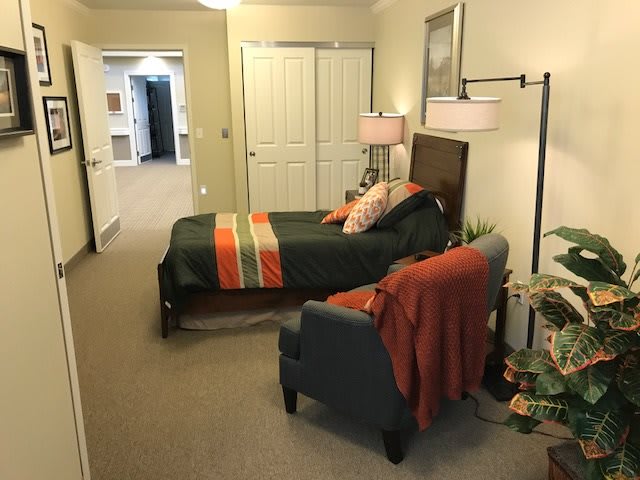 A cozy bedroom featuring a bed with colorful bedding, a comfortable chair, and warm lighting.