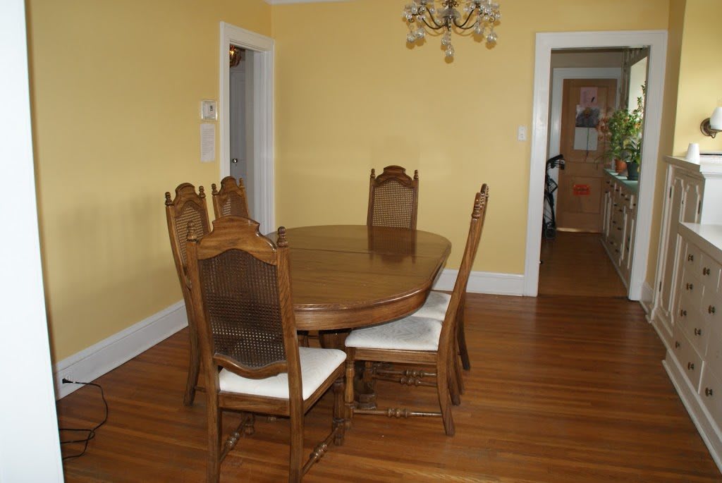 A dining room with a wooden table and four chairs, featuring a chandelier and hardwood flooring.