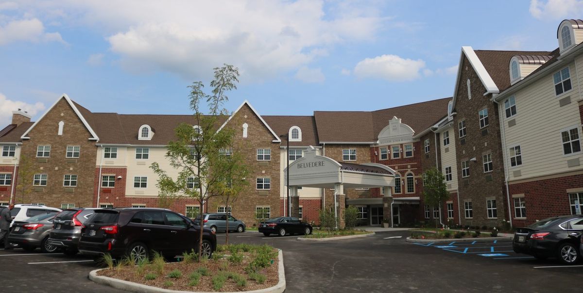 A residential building with a parking lot and landscaped surroundings on a cloudy day.