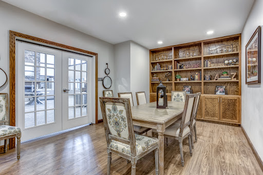 A cozy dining room featuring a wooden table, floral chairs, and a well-stocked bookshelf.