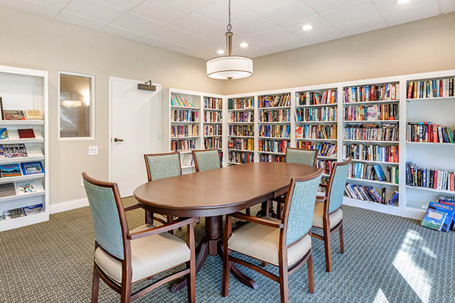 A cozy library meeting room with bookshelves lining the walls and a central table surrounded by chairs.