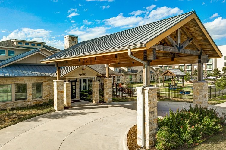 Modern building entrance with a covered walkway and stone pillars on a sunny day.