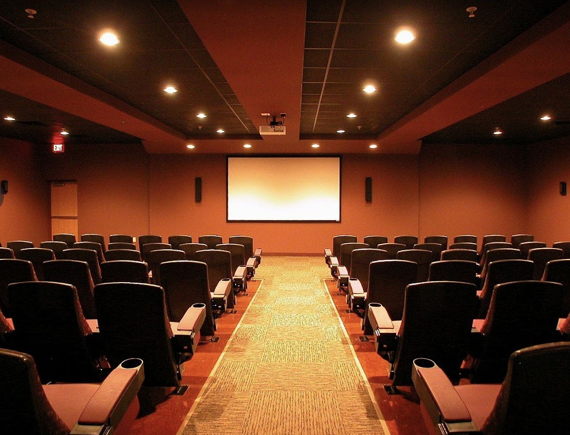 An empty theater with rows of seats facing a large screen.