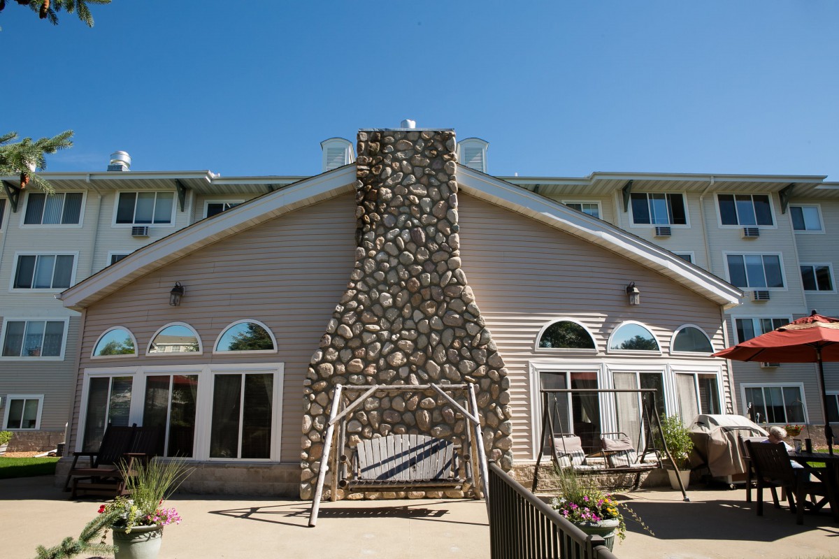 A house with a prominent stone chimney, featuring a swing and outdoor seating on the patio.