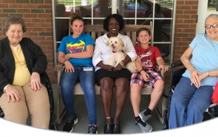 A group of people sitting together on a bench with a dog.