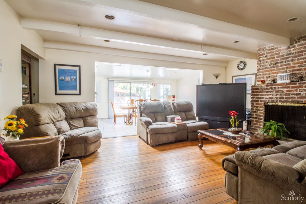 A cozy living room featuring plush sofas, a large TV, and wooden floors, complemented by natural light.