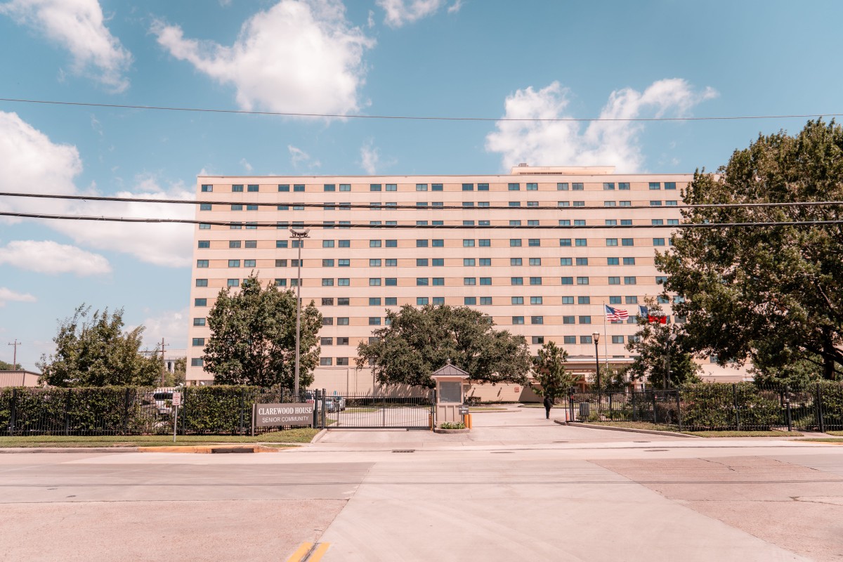 A tall apartment building with a gated entrance under a partly cloudy sky.