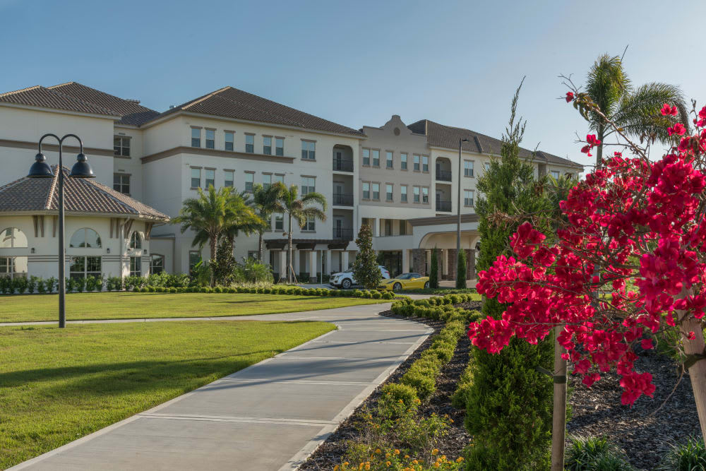 A beautiful residential building surrounded by a well-maintained landscape with vibrant flowers and palm trees on a sunny day.