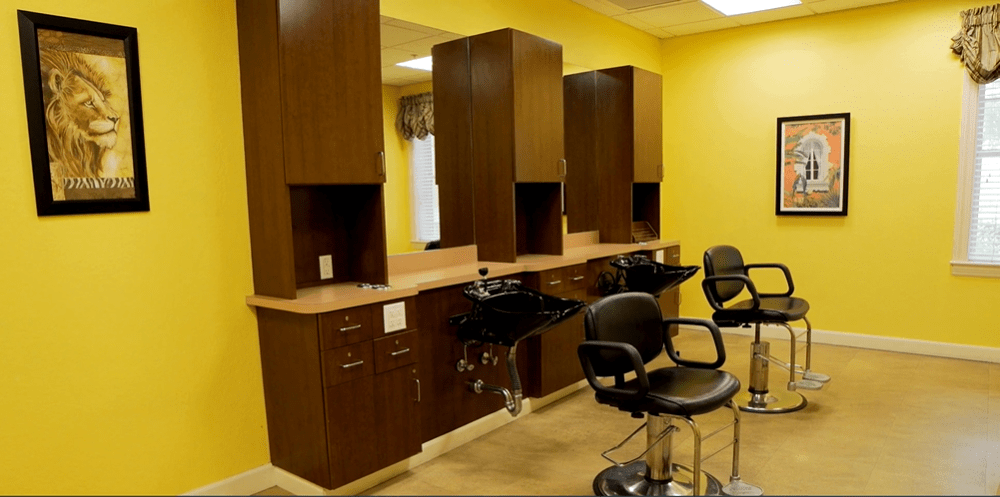Empty hair salon with styling chairs and sinks in a bright yellow room.
