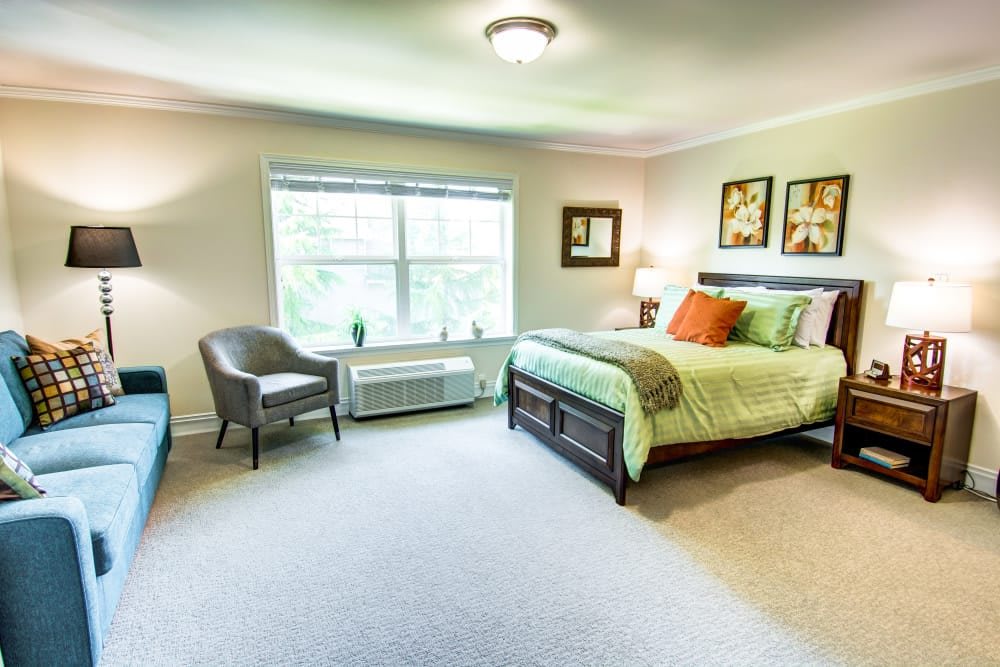 A well-lit bedroom featuring a comfortable bed, armchair, and decorative artwork.