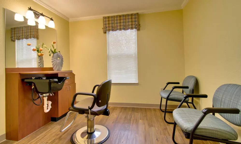 A cozy salon interior with styling and waiting chairs, yellow walls, and a window.