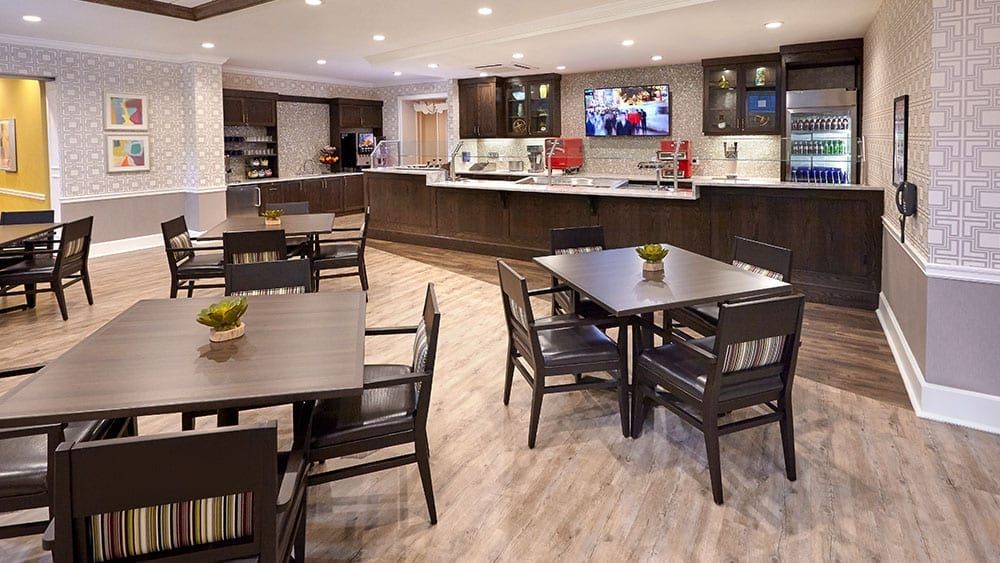 A modern dining area with tables and chairs, featuring a kitchenette and television.