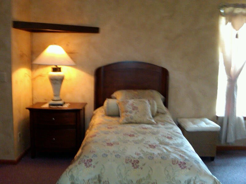 A cozy bedroom with a single bed, lamp, and nightstand.