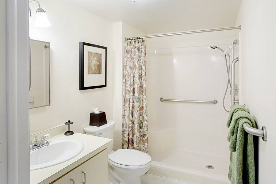 A clean and simple bathroom with a shower and curtain, sink, toilet, and mirror.