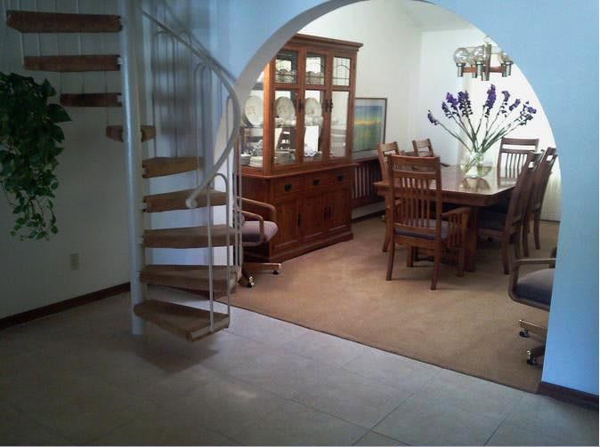 A cozy dining room featuring a wooden table and chairs, with a spiral staircase leading to an upper level.