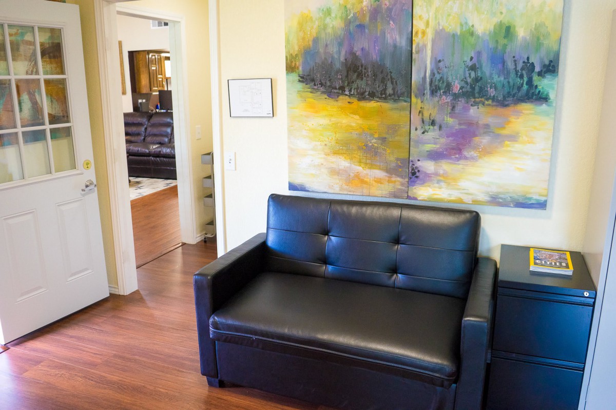A modern office waiting area featuring a black leather sofa and colorful abstract artwork on the wall.