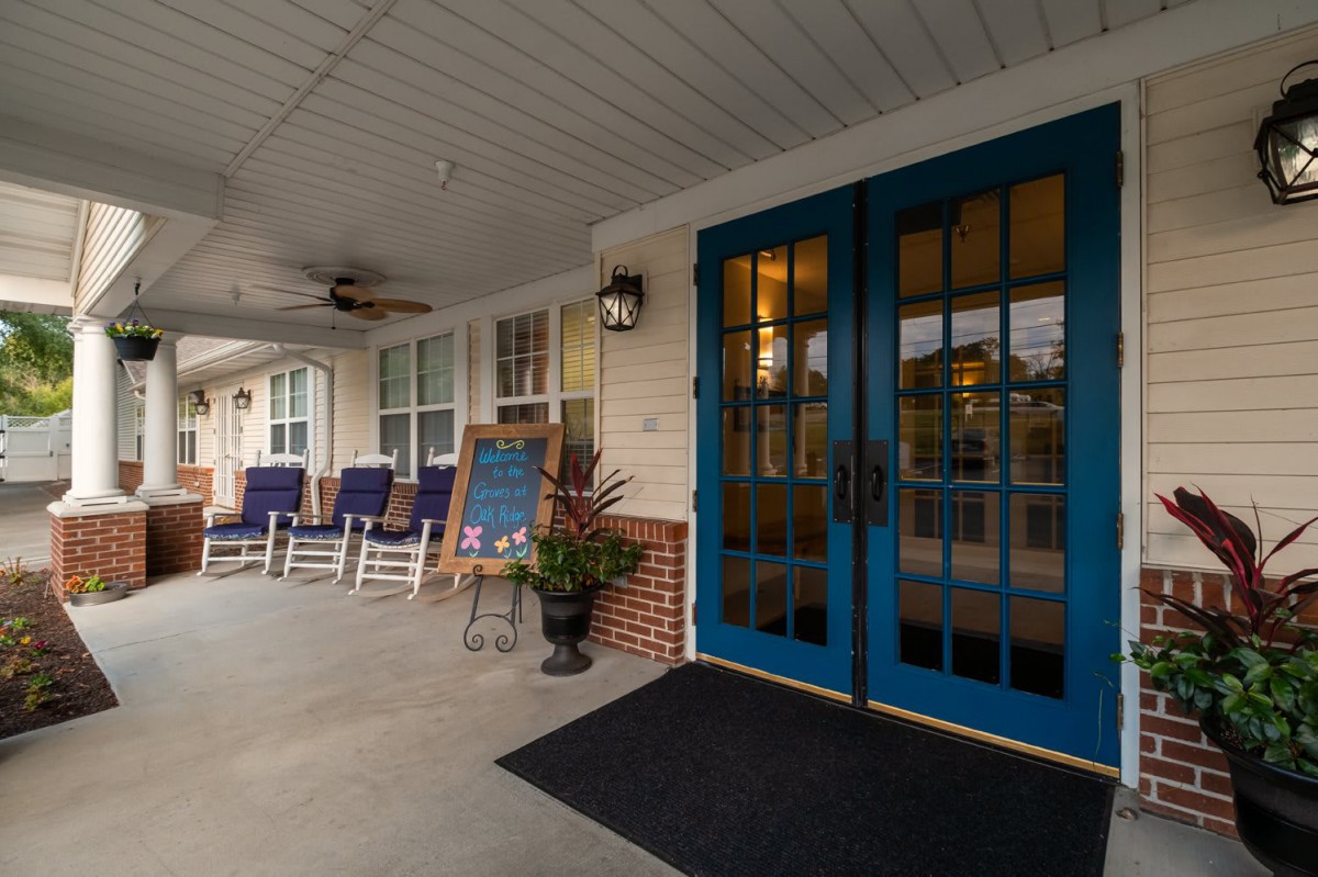 A cozy front porch with blue doors, rocking chairs, and a chalkboard sign.