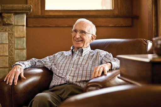 An elderly man sitting comfortably in a chair, smiling.