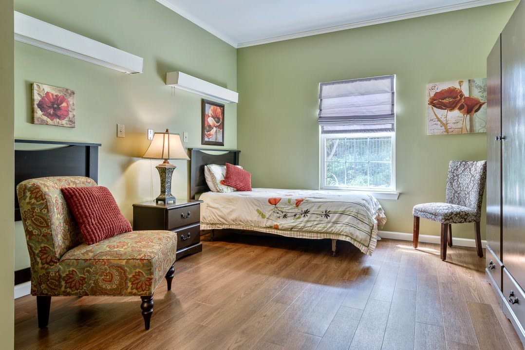 A cozy bedroom with a single bed, soft lighting from a lamp, and green-painted walls.