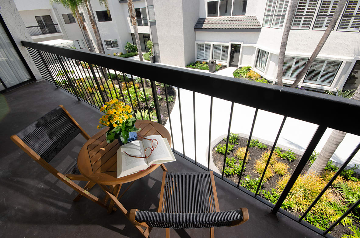 A cozy apartment balcony with a small table, a book, and flowers overlooking a residential courtyard.