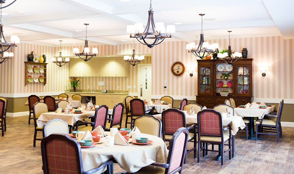 A well-decorated restaurant dining room with tables set for service and elegant chandeliers hanging from the ceiling.