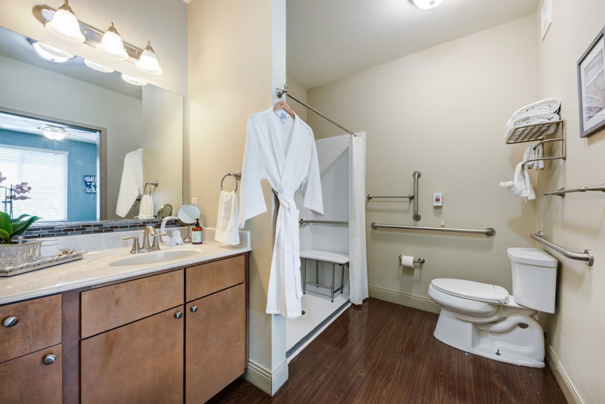 A modern bathroom featuring a robe, sink with mirror, and toilet.