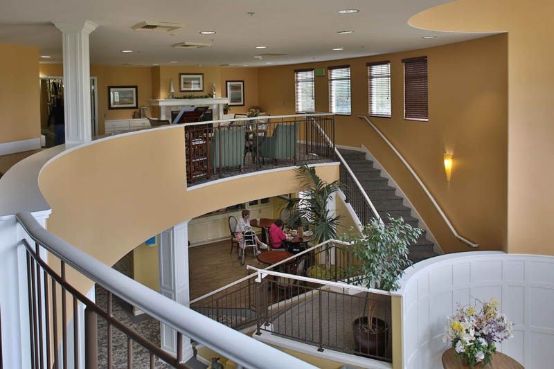 A spacious interior with a curved staircase and balcony, featuring comfortable seating and decorative plants.