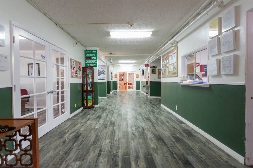 A spacious hallway with green walls and fluorescent lighting leads to various offices.