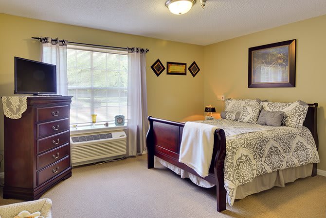A cozy bedroom with a large bed, dresser, and a window letting in natural light.