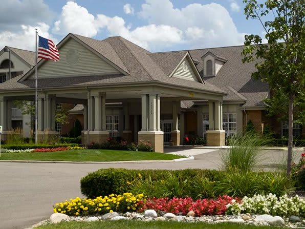 A well-maintained building entrance with colorful landscaping and an American flag.
