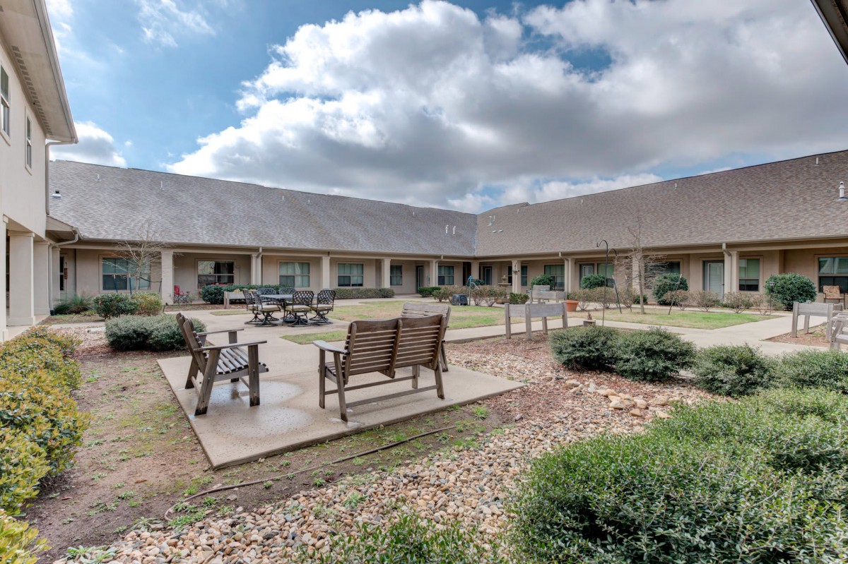 A serene courtyard with benches and a well-maintained garden under a partly cloudy sky.
