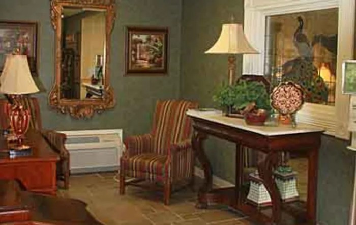 A cozy living room with elegant furniture and decor, featuring a striped armchair, ornate mirror, and a table with a lamp and plants.