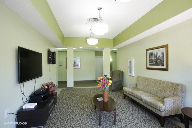 A well-lit living room featuring a sofa, wall-mounted television, coffee table with flowers, and tasteful decor.