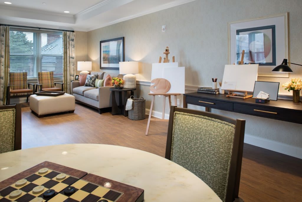 A well-lit living room featuring a cozy sofa, a chess board on the table, and art supplies set up for creative activities.