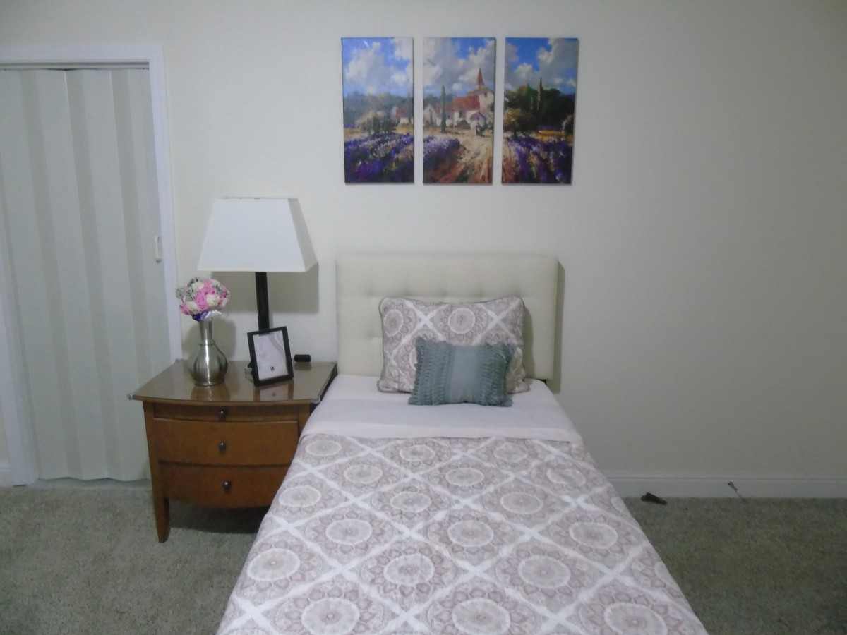 A neatly arranged bedroom with a single bed, nightstand, and decorative artwork on the wall.