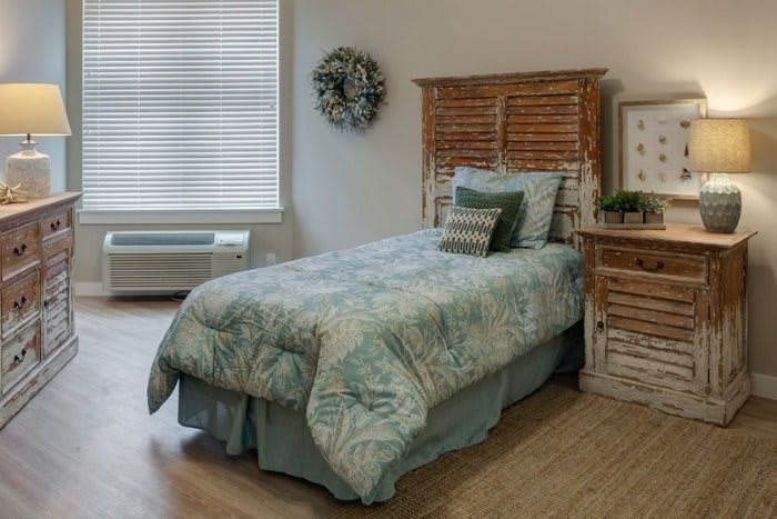 A cozy bedroom featuring a single bed with a blue patterned quilt, accented by a rustic wooden headboard and a wreath on the wall.