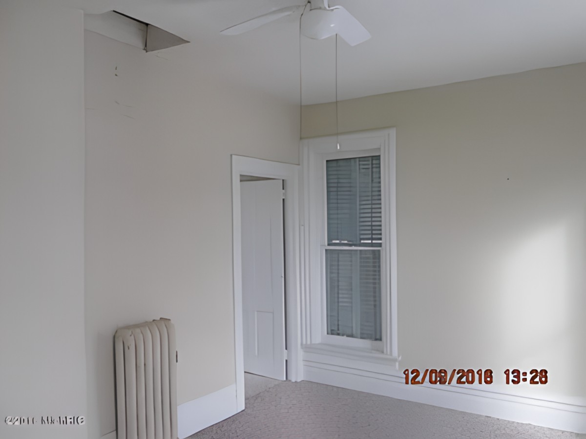 An empty room with a window, door, radiator, and ceiling fan.