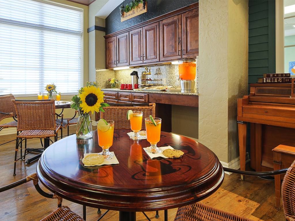 A cozy kitchen interior with a round table featuring three glasses of orange drinks and a sunflower centerpiece.