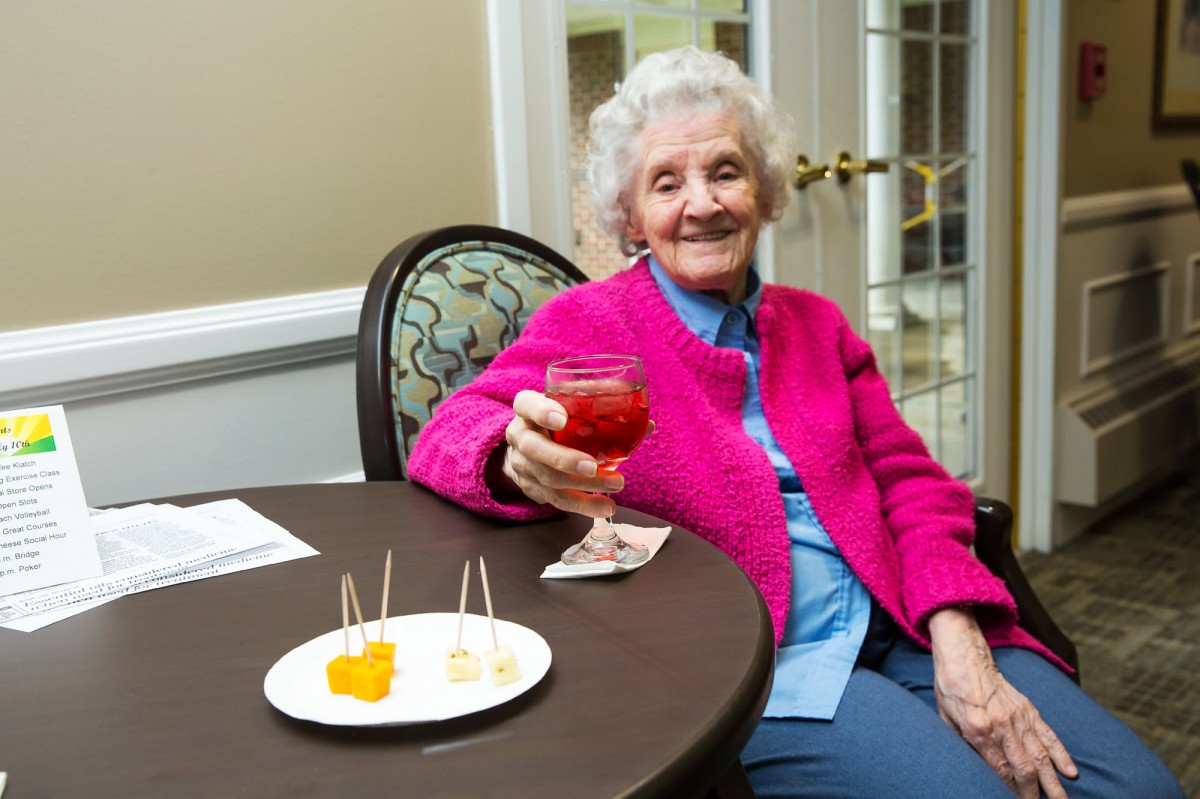 An elderly woman smiles while holding a drink at a social gathering.