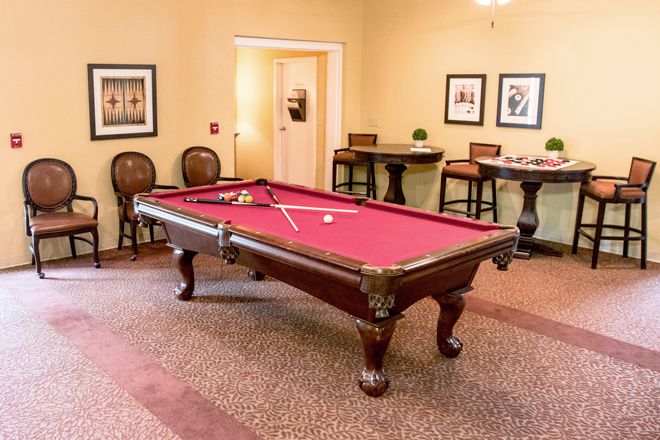 A cozy game room featuring a classic pool table with a red felt top, surrounded by elegant seating and wall art.