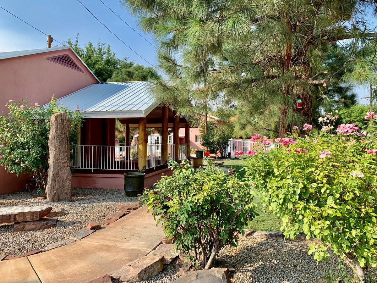 A quaint house with a front porch surrounded by lush greenery and a stone pathway on a sunny day.