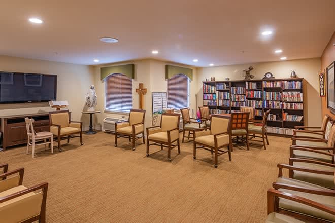 A cozy meeting room with arranged chairs, bookshelves, and a cross decoration.