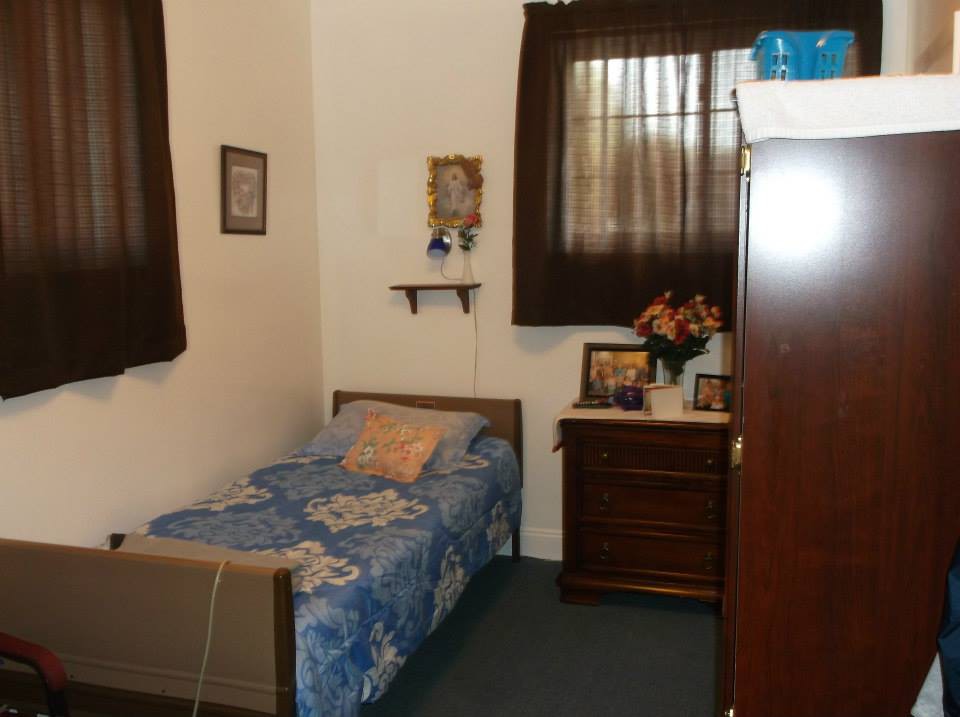 A simple bedroom with a single bed, brown curtains, and a dresser adorned with flowers and framed pictures.