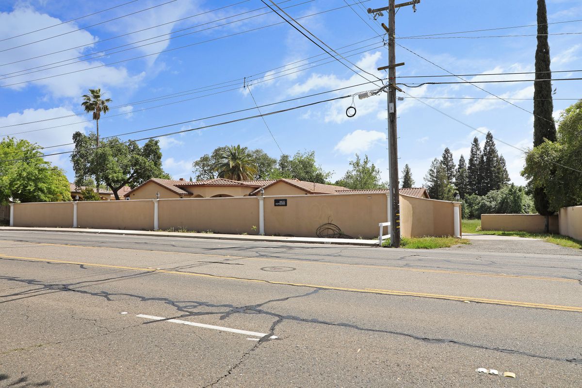 A residential building on a sunny day with visible power lines and trees along an asphalt road.