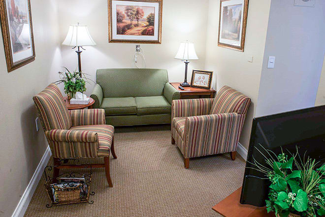 A cozy living room with a green sofa, striped armchairs, lamps, and wall art.