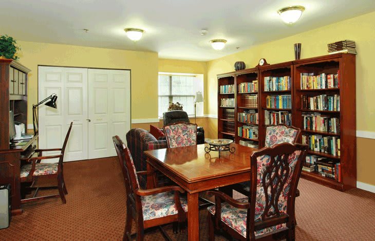 A cozy library room with bookshelves, a wooden table, and chairs.
