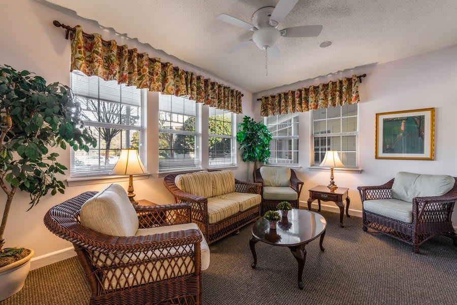 A cozy and well-lit living room with wicker furniture, large windows, and a ceiling fan.