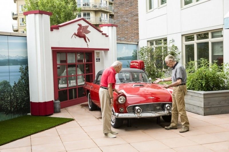 Two men examining a vintage red car in front of a garage with a Pegasus logo.