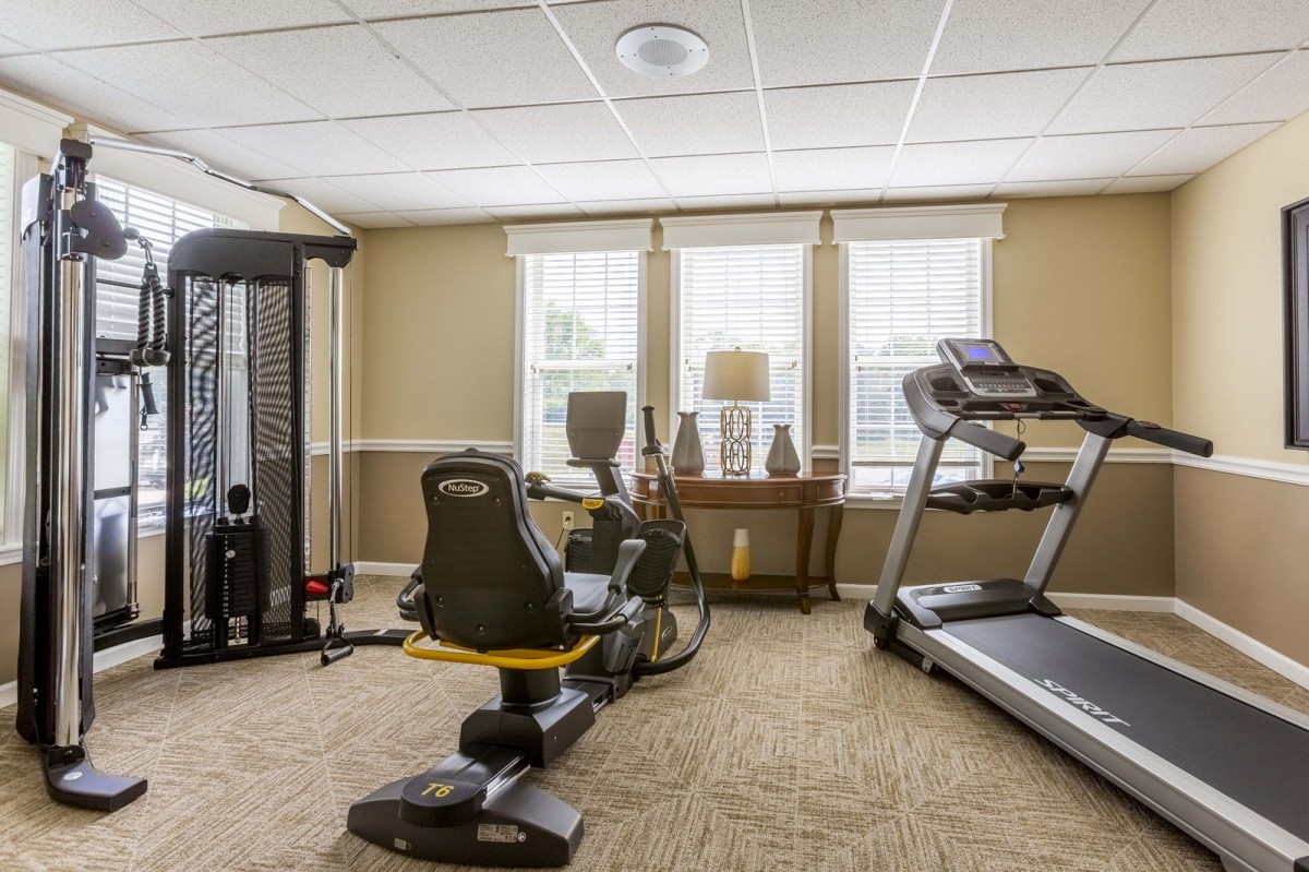 A well-lit fitness room with various exercise equipment, including a treadmill, stationary bike, and weight machine.