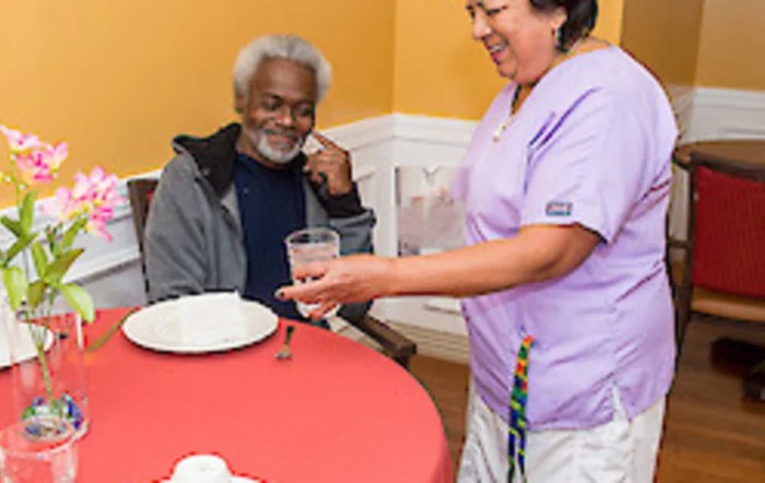 A caregiver assists an elderly man during mealtime.